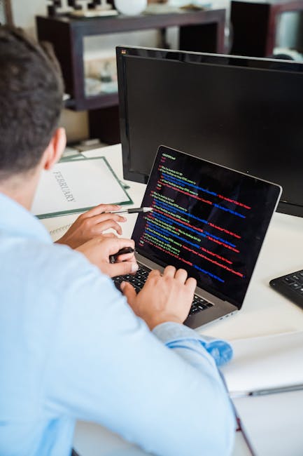 Close-up of a computer screen displaying lines of programming code with syntax highlighting in various colors, including orange, yellow, pink, green, and white on a dark background. The code features 